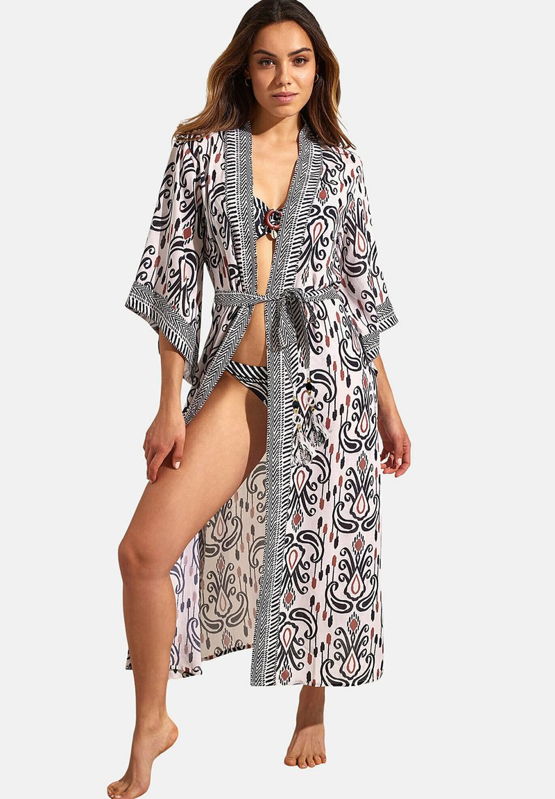 Lange, lichte cover-up in het roze met zwarte en rode patronen, kimono-mouwen en een gestrikte taille. Heeft een diepe opening aan de voorkant.