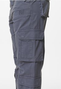 Námořnické cargo kalhoty mají několik bočních kapes, odolnou tkaninu a viditelné švy, což skýtá utilitární design.