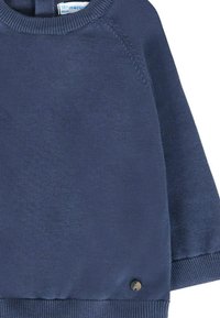 Maglione lavorato a maglia blu navy con scollatura rotonda, polsini e orlo a coste. Presenta un piccolo dettaglio con bottone nero vicino all'orlo.