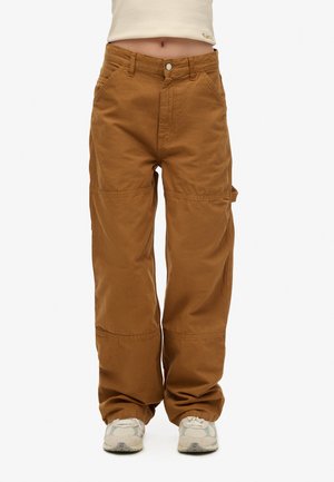 Pantalones cargo marrones de corte holgado, con cierre de botón, bolsillos laterales y detalles de costura visibles. Combinados con zapatillas de color claro.