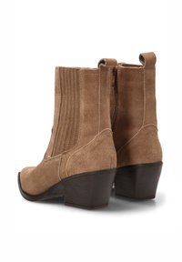 Botas de tobillo de ante marrón con un tacón curvado, detalles estriados en los lados y una cremallera trasera. Diseño de punta redonda; textura suave.