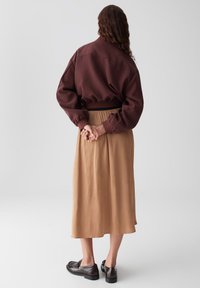 Felpa oversize marrone con orlo a coste, abbinata a una gonne midi beige fluida. Scarpe nere completano l'outfit. Vista da dietro.