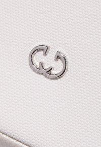 Tessuto bianco texturizzato con un logo "G" intrecciato in argento. Superficie liscia con un motivo sottile, che mette in risalto la finitura lucida del logo.