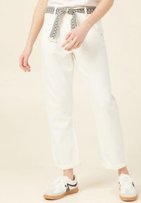 Pantaloni in denim bianco con una cintura tessuta a motivo e i risvolti, abbinati a sneakers grigie e bianche. Focalizzazione su un look casual e rilassato.