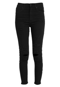 Jeans ajustados de tiro alto en negro con detalles desgastados, que presentan múltiples desgarrones y una tela delgada y elástica para un ajuste ceñido.