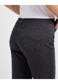 Černé džínsy z denimu z pohledu zezadu, s jemným vlnkovým prošíváním na kapsách a malou značkovou visačkou poblíž pásu.