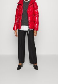 Chaqueta acolchada roja brillante con capucha, suéter gris debajo, camisa blanca, pantalones negros y mules negros de tacón. Estilo minimalista.