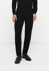 Schwarze Jogginghose im Slim-Fit-Design, ausgestattet mit einem elastischen Bund und Zugband, aus weichem Stoff mit glatter Textur.