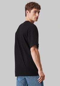 T-shirt nera a maniche corte con scollatura rotonda, caratterizzata da una vestibilità rilassata e una texture del tessuto liscia. Indossata con jeans blu.