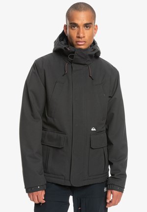 Veste imperméable noire avec capuche, deux poches avant et un patch logo. Le matériau est lisse avec une finition mate, et le design est utilitaire.