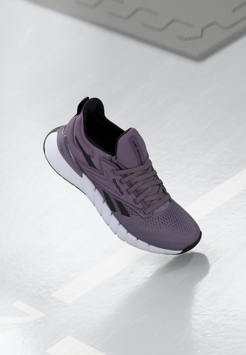 Μωβ αθλητικό παπούτσι με αναπνεύσιμο πλέγμα στην πάνω μεριά, μαύρες λεπτομέρειες και λευκή ευλύγιστη σόλα με έντονες αυλακώσεις για πρόσφυση.