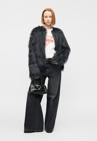 Μαύρο μπουφάν από ψεύτικη γούνα, λευκό πουκάμισο με κόκκινο τύπωμα, μαύρο τζιν ψηλόμεσο και μικρή μαύρη τσάντα με μεταλλικές λεπτομέρειες.