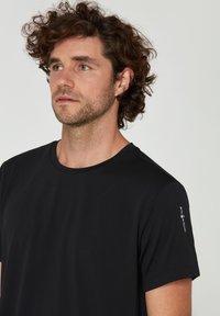 Sort kortærmet t-shirt lavet af blødt stof. Har en rund halsudskæring og et logodetalje på venstre skulder. Glat tekstur.