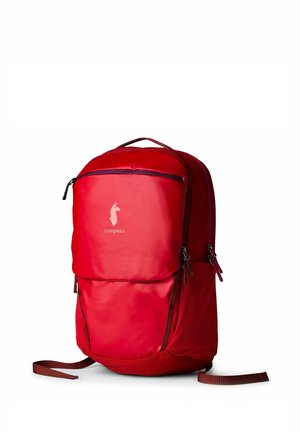Mochila Cotopaxi de color rojo brillante con varios compartimentos con cremallera y correas ajustables, colocada en posición vertical sobre un fondo blanco.