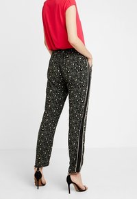 Zwarte broek met een luipaardprint, tapered fit en zijstrepen. Gepaard met een rode top en hoge hakken.