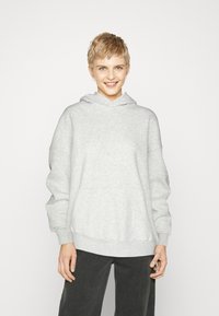 Hanorac gri deschis cu glugă reglabilă, umeri căzuți și buzunar frontal. Textură moale, croială lejeră, asortat cu pantaloni închiși la culoare.