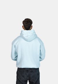 Felpa con cappuccio azzurro chiaro dal taglio morbido, caratterizzata da un grande cappuccio e un tessuto testurizzato, abbinata a jeans grigio scuro.