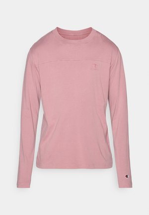Chemise rose clair à manches longues en coton. Présente un col rond et un petit logo sur la poitrine et la manche. Texture douce, design minimaliste.
