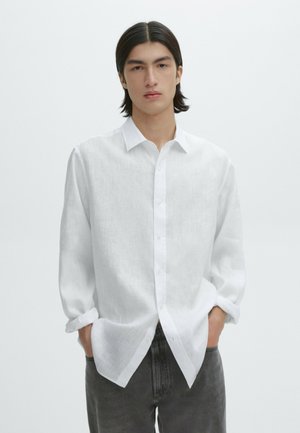 Witte linnen blouse met een button-down kraag, lange mouwen en een relaxte fit. Gecombineerd met grijze denim broek. Minimalistisch ontwerp.
