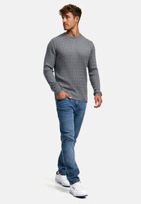 Grå kabelstrikket genser med rund hals, lange ermer, sammen med lyseblå jeans og hvite sneakers, som viser et avslappet antrekk.