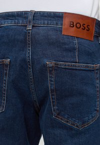 Σκούρο μπλε τζιν από denim, πίσω όψη που δείχνει διπλές τσέπες και ένα καφέ δερμάτινο ταμπελάκι με την ένδειξη BOSS στη μέση.