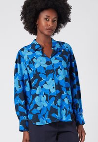 Niebieska bluzka w kwiatowy wzór na granatowym tle, z przodu zapinana na guziki i długimi rękawami. Wykonana z lekkiego materiału o gładkiej teksturze.