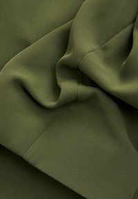 Tela de color verde oliva, texturada y con un sutil patrón acanalado, drappeada y arrugada, mostrando suavidad y flexibilidad.