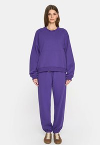 Fioletowy zestaw składający się z bluzy i spodni. Bluza ma okrągły dekolt i luźny krój. Spodnie mają elastyczny pas i mankiety.