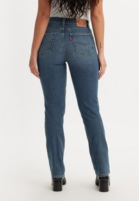 Temno modri visokokvalitetni jeans s ravnim nogavicami, ki imajo usnjen znak na hrbtni strani in klasične zadnje žepe. Gladek denim material.