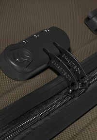 Combinatieslot dat twee zwarte ritssluitingen met het label "SMARTBOX" op bruin gestructureerd bagagestof beveiligd.