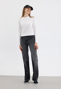 Langermet hvit topp kombinert med løstsittende mørkegrå jeans og svarte sneakers, supplert med en svart baseballcap.