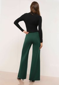 Melnā ribota garo piedurkņu krekls ar augstu kaklu, saskaņots ar plaša piegriezuma zaļām biksēm. Biksēm ir gluda tekstūra un precīza piegriezuma forma.