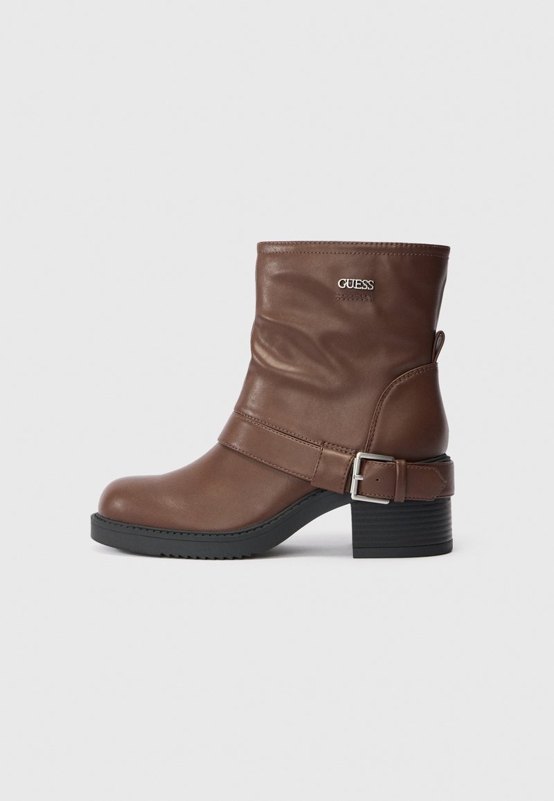 Bottines en cuir marron avec un design fléchi, un accent de boucle sur le côté et un petit talon empilé avec une semelle en caoutchouc texturé.