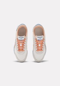 Zapatillas blancas con parte superior de malla y ante, cordones melocotón, acentos en azul y suela texturizada. Presenta el logo de Reebok en la lengüeta.