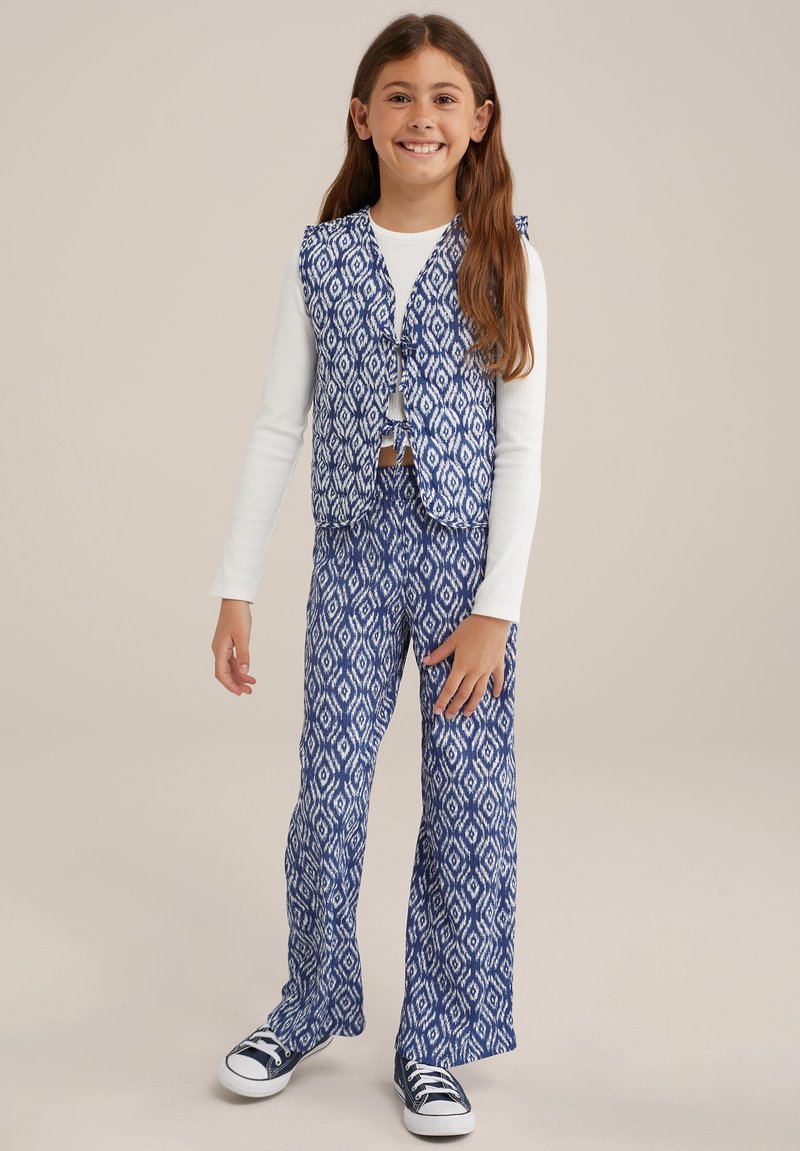 Kaksiosainen asu, jossa on sinivalkoinen kuvioitu hihaton liivi ja leveälahkeiset housut. Kankaan pinnassa on teksturoitu, kudottu ilme.