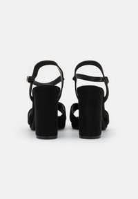 Sandali neri in scamosciato con tacco a blocco e cinturini alla caviglia regolabili, design con punta aperta. I tacchi sono alti circa 10 cm.