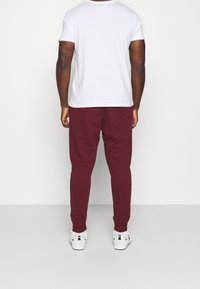 Vit T-shirt med kort ärm, vinröda mjukisbyxor och vita sneakers. Byxorna har en avsmalnande passform, slät textur och elastiska muddar vid anklarna.