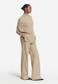 Beige ribbad polotröja med sidfickor, parat med vida beige byxor och svarta spetsiga skor. Slät textur, avslappnad passform.