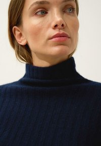 Granatowy sweter z golfem wykonany z ribbowanego materiału, z wysokim kołnierzem i subtelną teksturą. Zbliżenie na obszar kołnierza.
