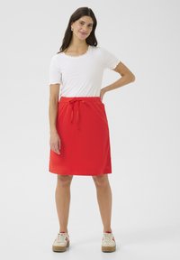 Röd knälång kjol med dragsko i midjan; parat med en vit kortärmad topp med scalloped halsringning; bärs med beige sneakers.