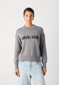 Hallhalli hallidega sügisjope, millel on must "calvin klein" kiri rinna kohal; lõdvestunud lõige ja ümmargune kaelus.