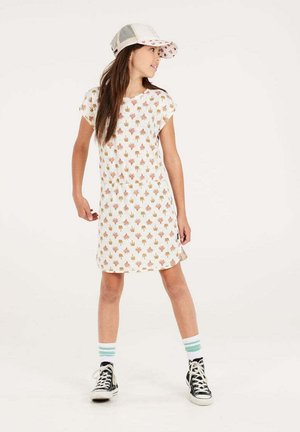 Weißes kurzes Kleid mit buntem Palmenprint. Das Modell trägt eine Kappe und schwarze Sneakers mit weißen Schnürsenkeln, kombiniert mit mintgrün gestreiften Socken.