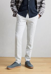 Ανοιχτό γκρι παντελόνια ραμμένα με κομψή υφή, σε συνδυασμό με ναυτικά παπούτσια με λαστιχένια σόλα. Το μοντέλο φοράει καρό πουκάμισο ανοιχτό στο γιακά.