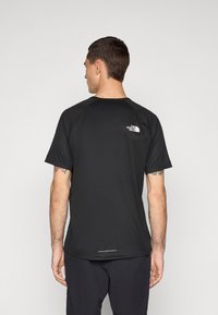 T-shirt esportivo preto com mangas curtas, tecido texturizado, decote redondo e um logo branco na parte superior das costas.