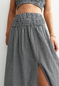 Black and white gingham patterned skirt with an elastic waistband, featuring a side slit and a soft, textured fabric.
