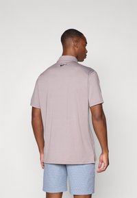 Svetlo šedé polo tričko s golierom a krátkymi rukávmi, s malým čiernym logom Nike na chrbte, skombinované s vzorovanými modrými šortkami.