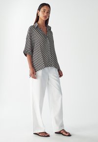 Košile s černobílým vzorem, volného střihu, s krátkými rukávy a límečkem, v kombinaci s bílými kalhotami rovného střihu a černými žabkami.