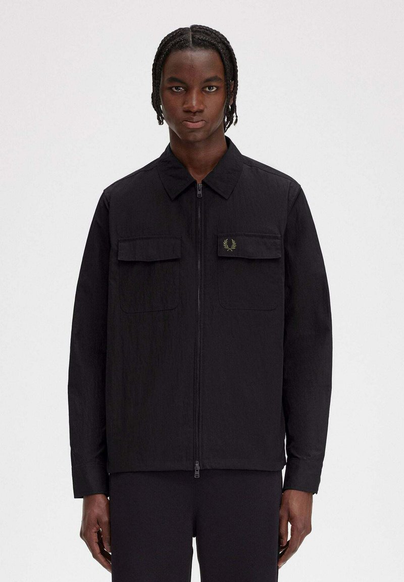 Giacca nera leggera con zip frontale, colletto e due tasche anteriori. Presenta una discreta patch con logo sulla parte sinistra del petto.