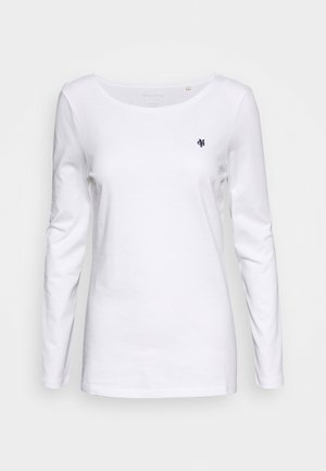 Camisa blanca de manga larga para mujer con cuello redondo y un pequeño logo oscuro en el pecho izquierdo, mostrada sobre un fondo claro y sencillo.