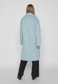Cappotto di lana azzurro chiaro con vestibilità rilassata, grande collo e maniche lunghe, caratterizzato da una consistenza morbida e un design di lunghezza intermedia.